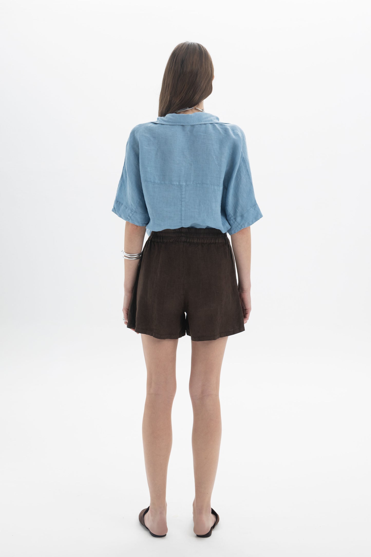 Back view of a model wearing a Linen Polo Top with brown shorts, showcasing the relaxed fit and lightweight fabric.