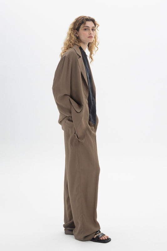 Model wearing Fluid Tailored Trousers with a relaxed fit and soft drape, styled with a dark shirt.