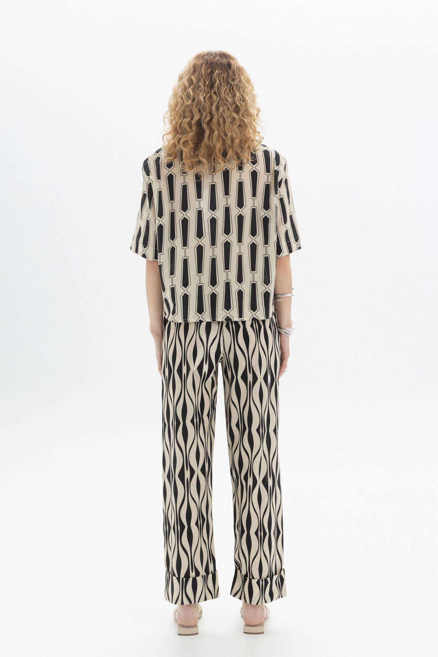 Back view of a woman wearing a Short Sleeve Shirt with bold geometric print and relaxed silhouette.
