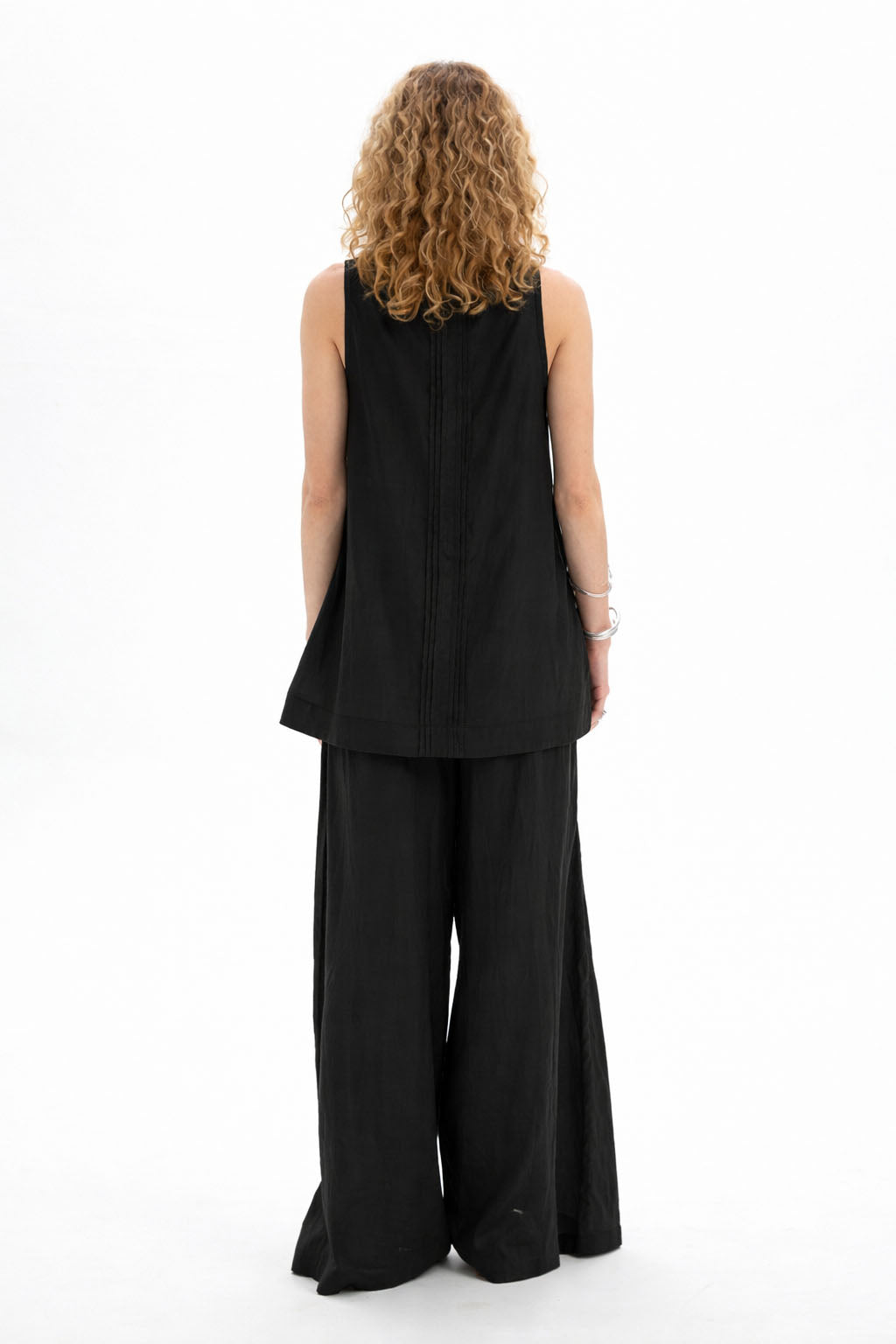 Back view of a model wearing a black sleeveless bib shirt paired with wide-leg pants.