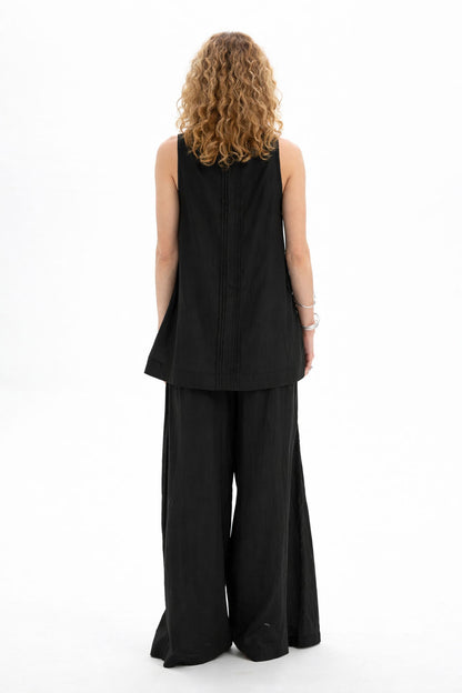 Back view of a model wearing a black sleeveless bib shirt paired with wide-leg pants.
