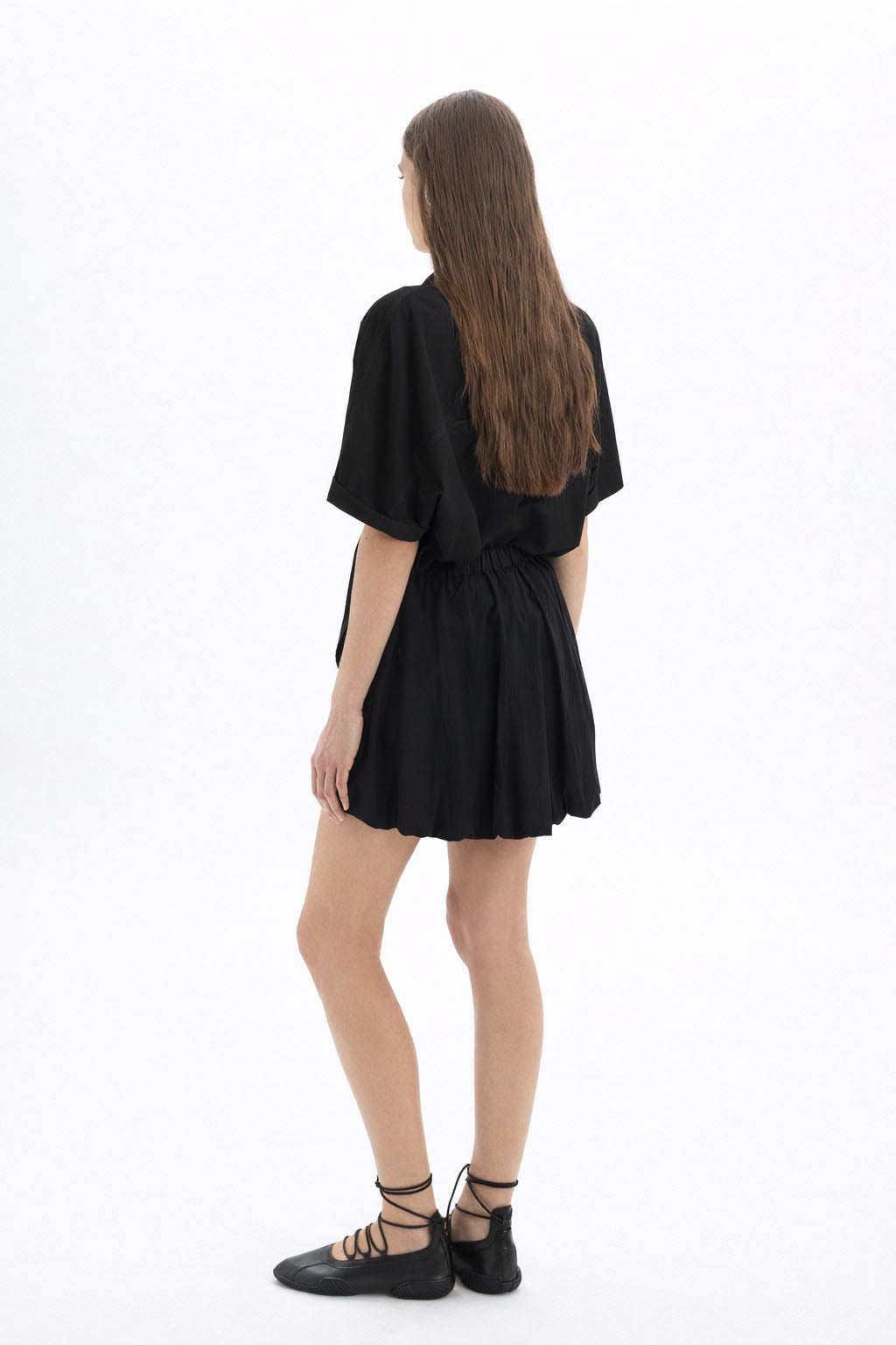 Cotton Short Sleeve Shirt worn with a black skirt, showcasing a relaxed-fit and modern silhouette from the back.