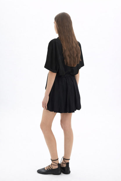 Cotton Short Sleeve Shirt worn with a black skirt, showcasing a relaxed-fit and modern silhouette from the back.