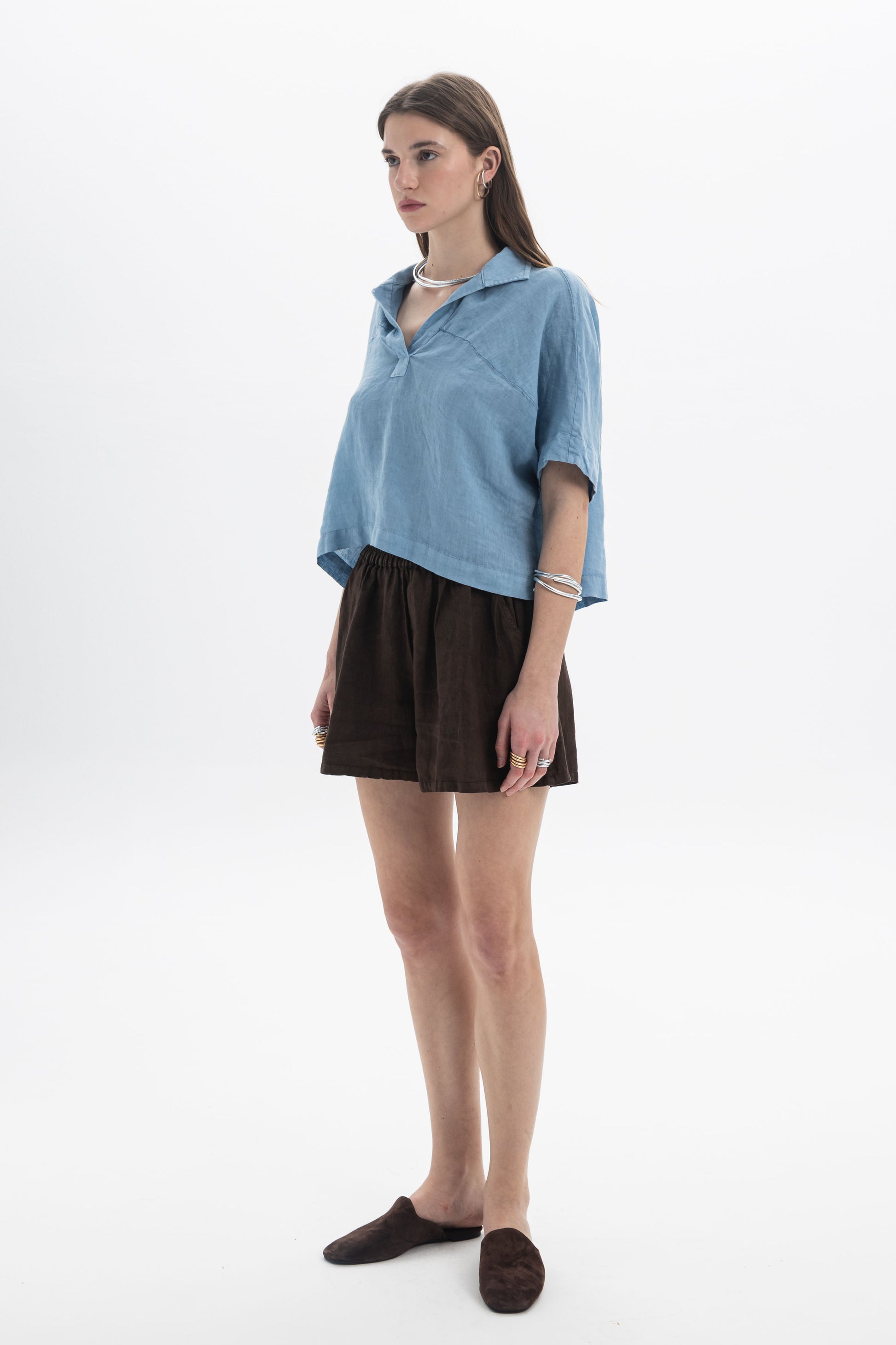 Model wearing a Linen Polo Top with relaxed silhouette and soft collar, paired with brown shorts.