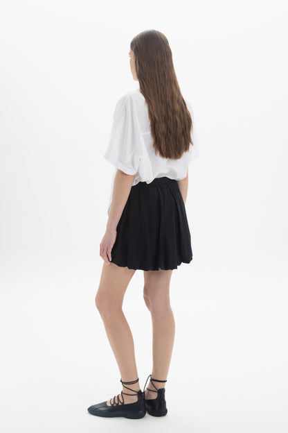Model wearing a Balloon Mini Skort with a white blouse, showing the back view and voluminous silhouette.