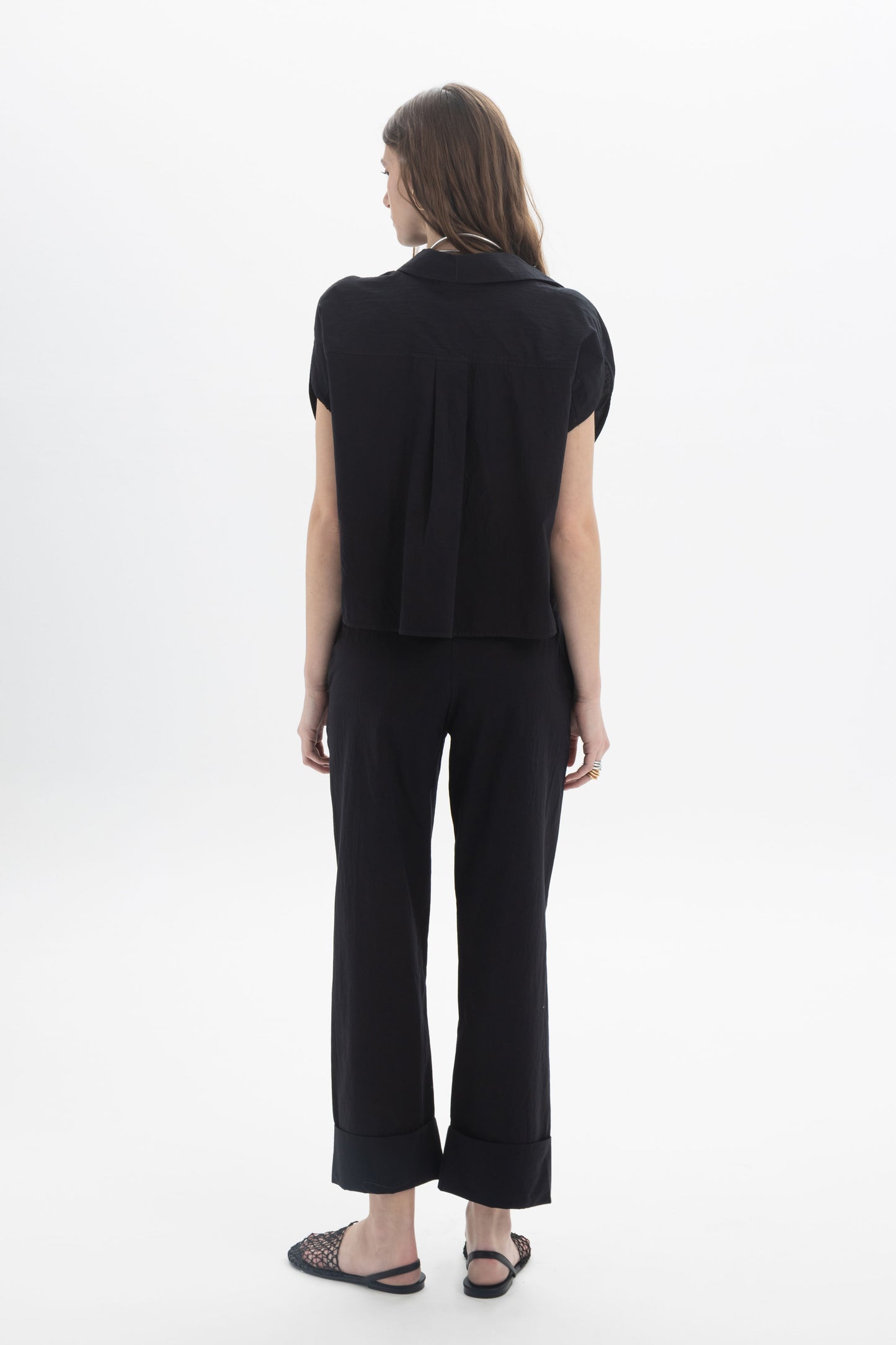 Model wearing a black Cropped Button Shirt from the back, paired with matching trousers, showcasing a minimal summer style.