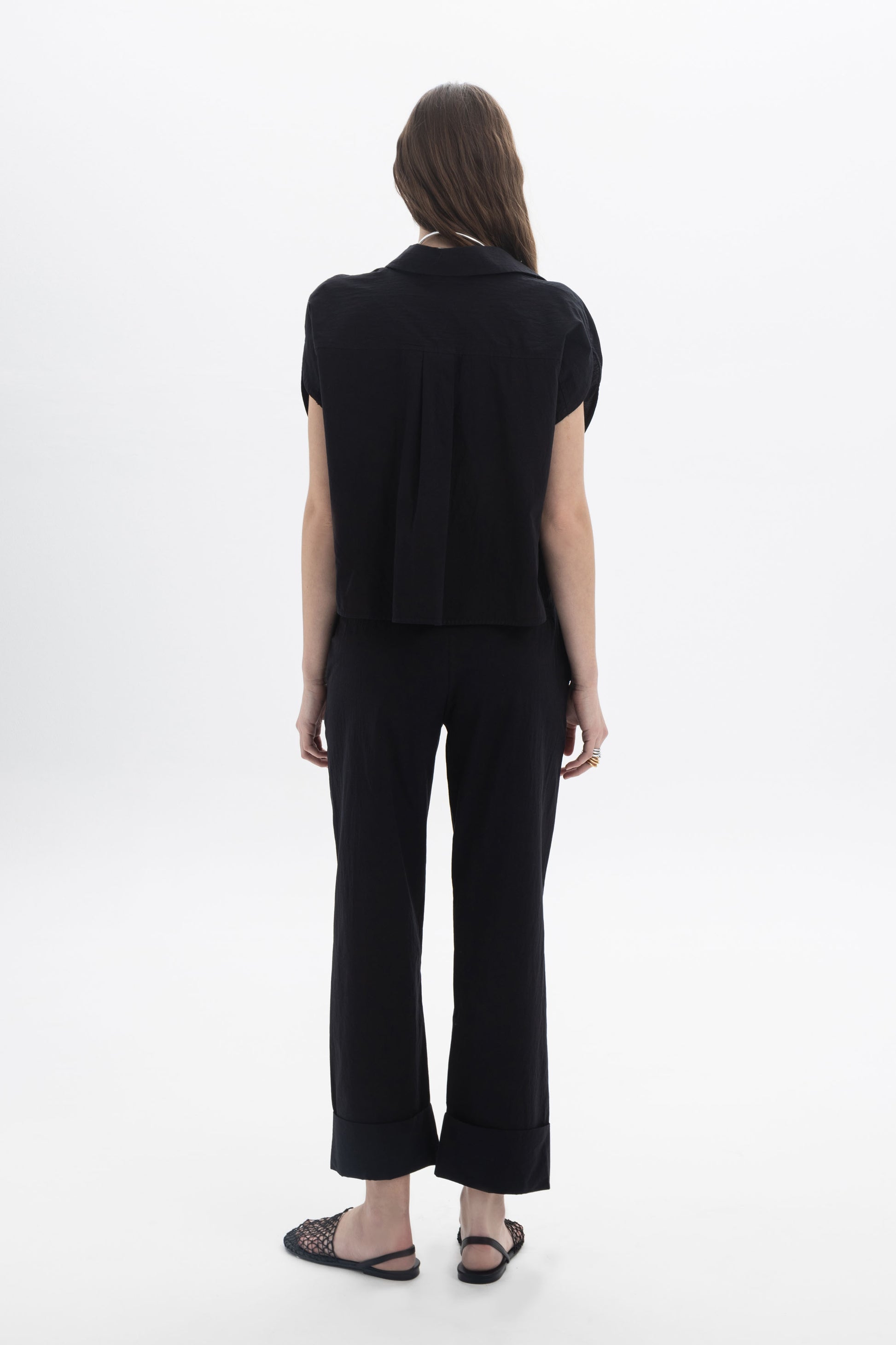 Back view of a model wearing a Cropped Button Shirt paired with black pants, showcasing modern summer style.