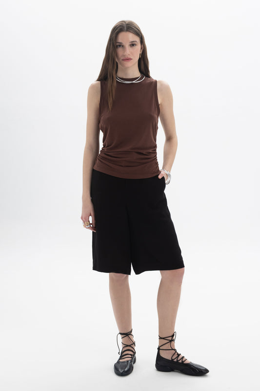 Ruched Sleeveless Top worn with black shorts, featuring side ruching and a high neckline for a contemporary look.