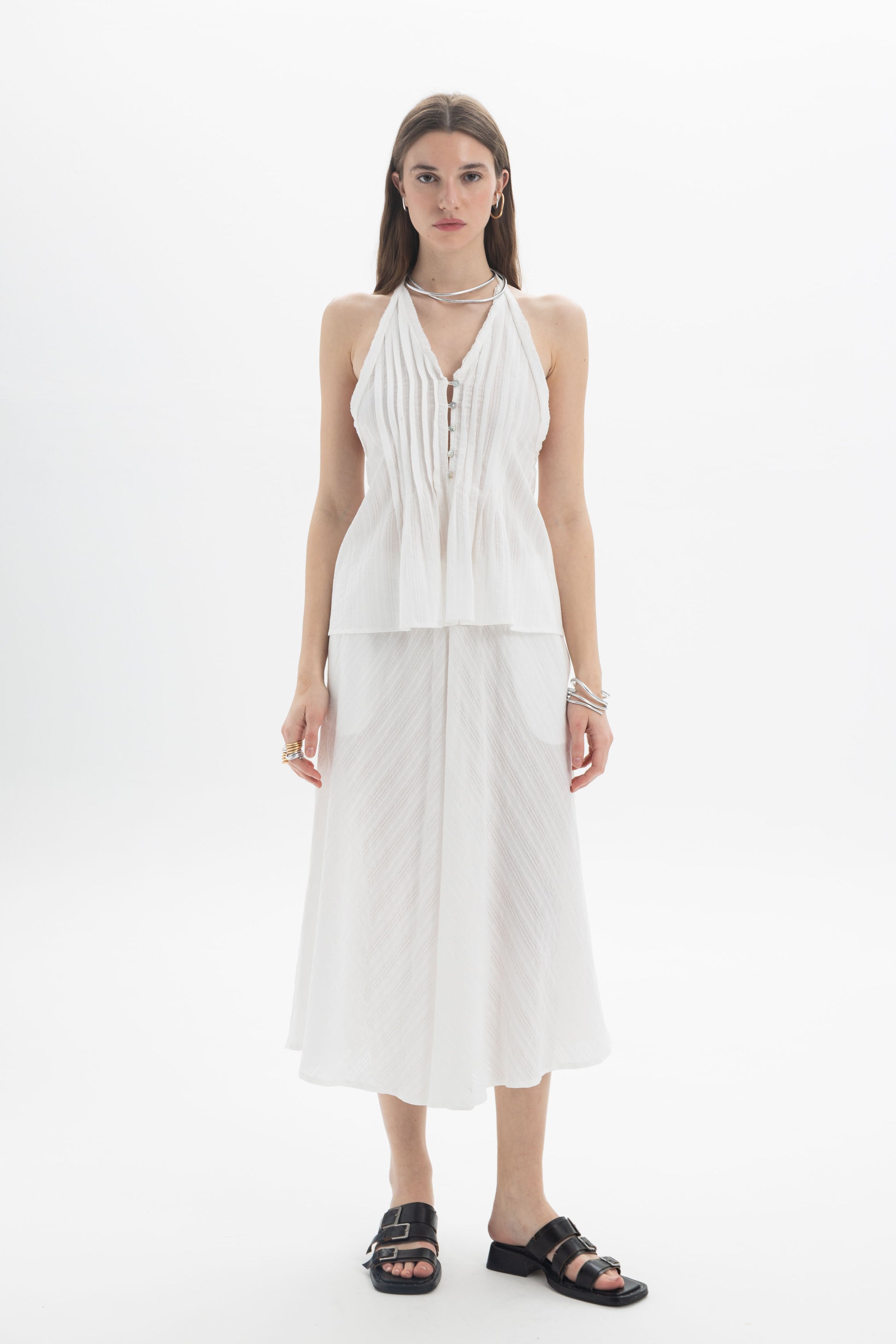 Model wearing a Pleated Halter Peplum Top with delicate pleats and flared silhouette, paired with a flowy skirt.