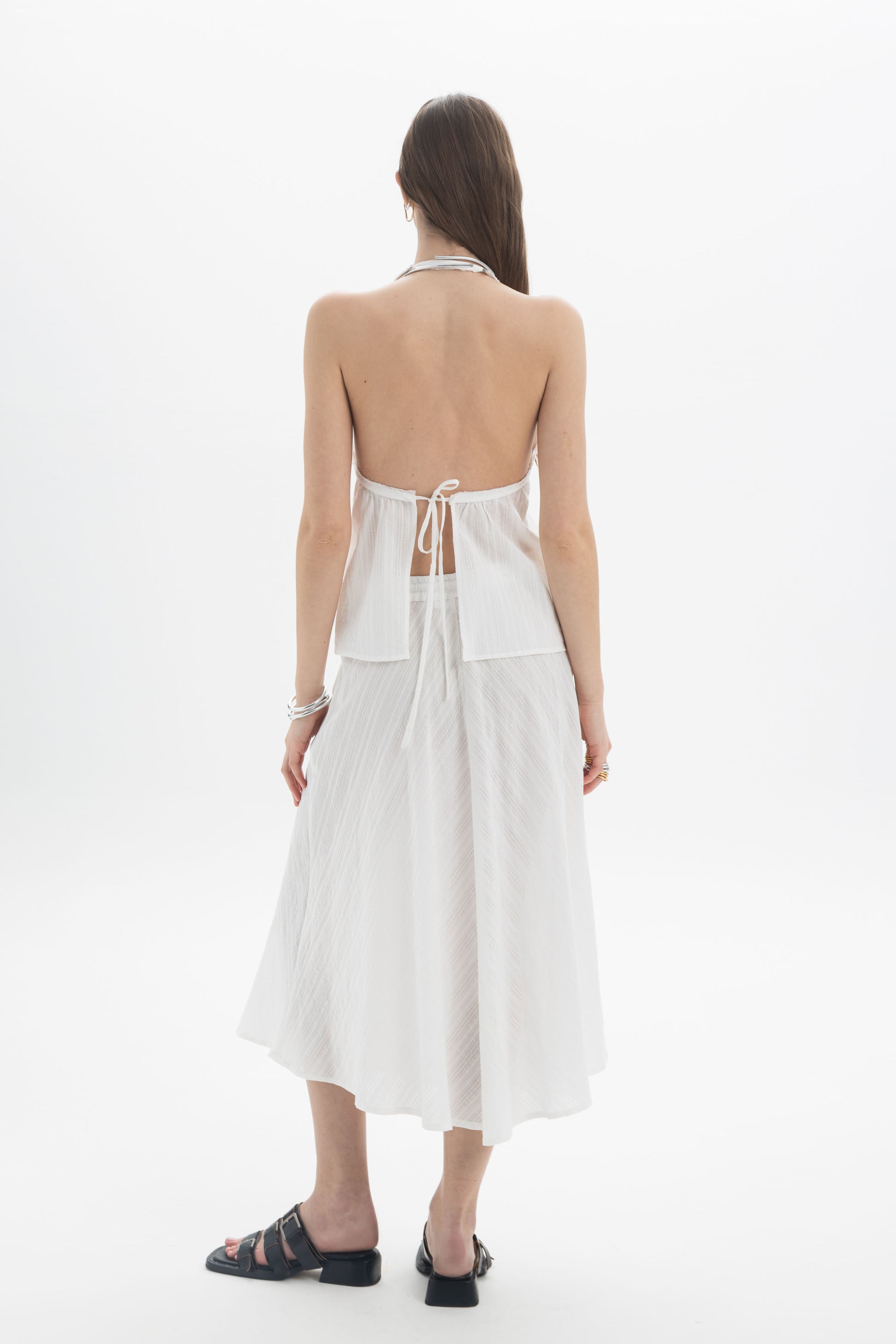 Back view of model wearing Pleated Halter Peplum Top with open back and tie detail, paired with a flowing skirt.