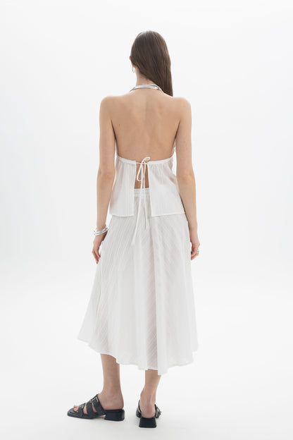 Back view of model wearing Pleated Halter Peplum Top with open back and tie detail, paired with a flowing skirt.