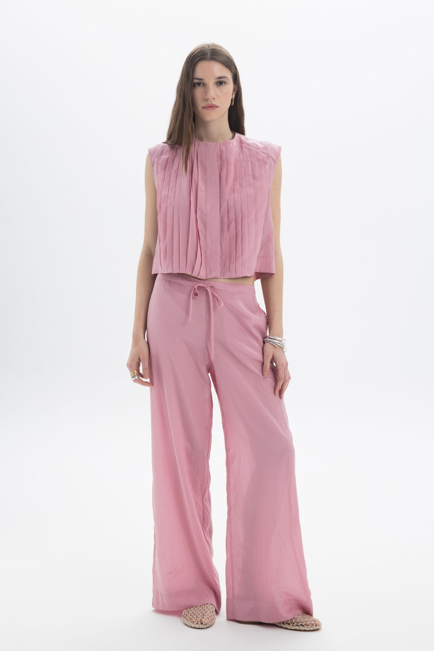 Pleated Cropped Sleeveless Top in soft pink with pleats, styled with relaxed trousers for a modern look.