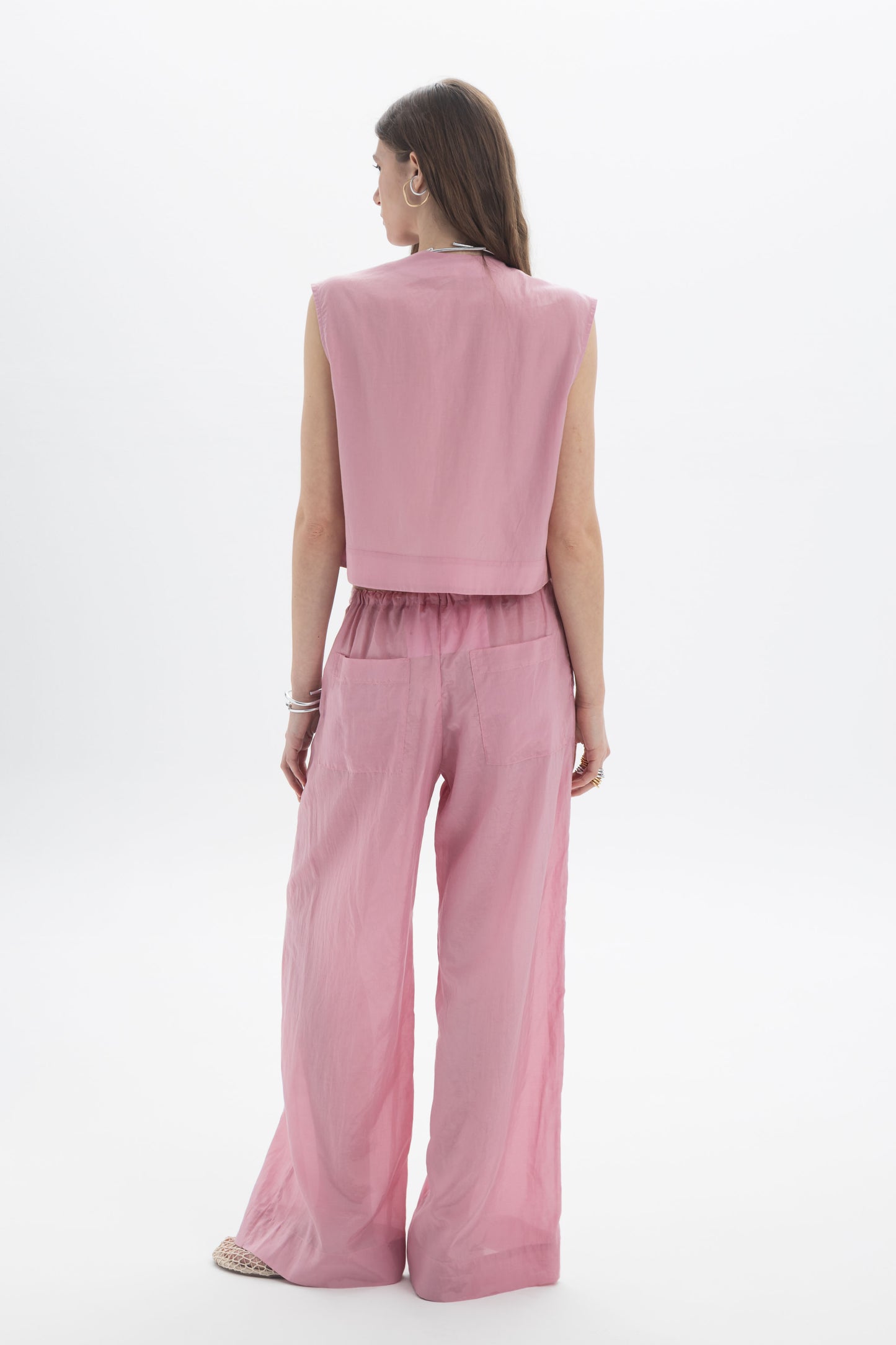 Pleated Cropped Sleeveless Top viewed from the back with relaxed trousers in soft pink fabric.