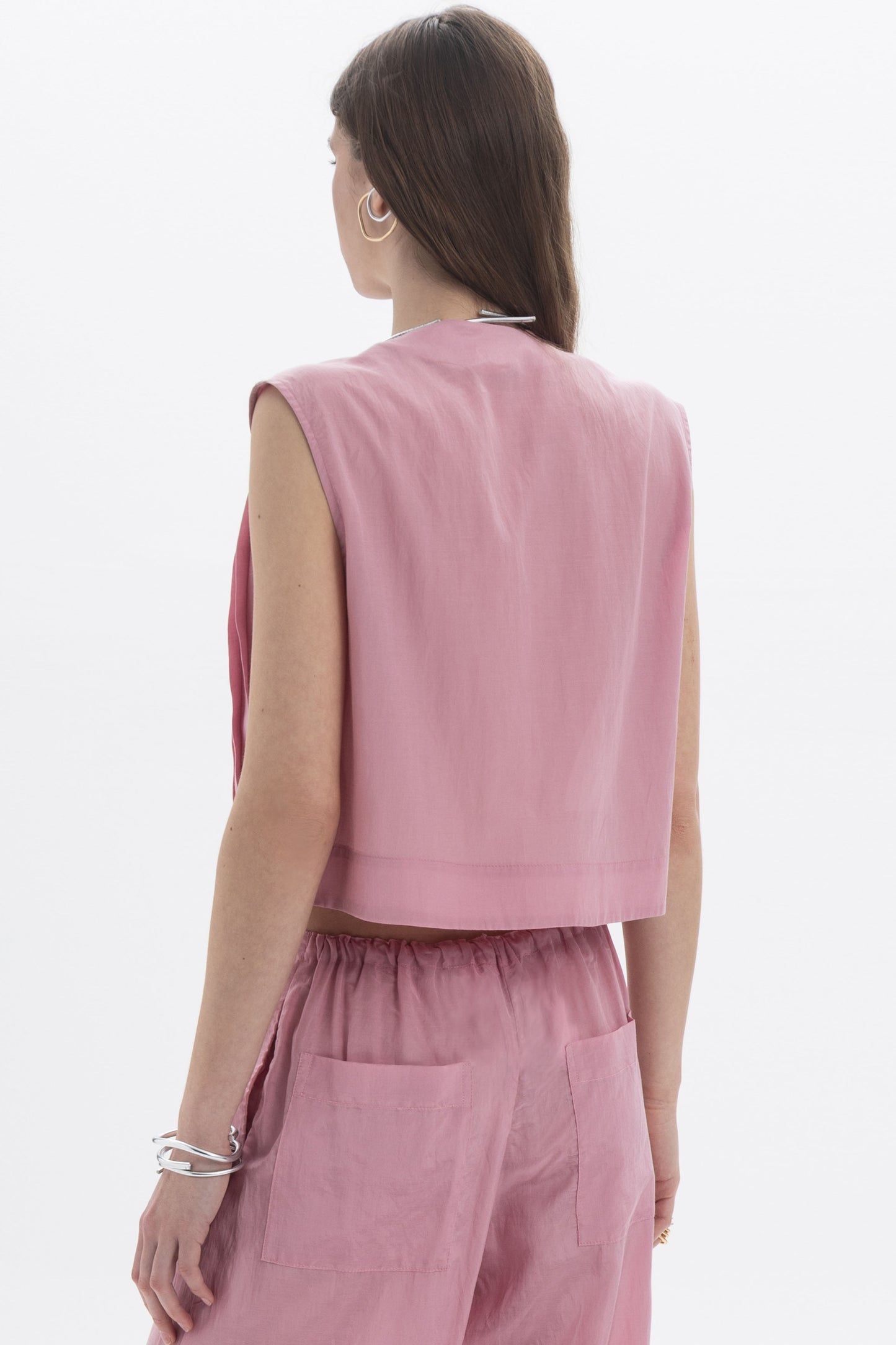 Back view of a woman wearing a Pleated Cropped Sleeveless Top in dusty pink, showcasing its modern silhouette.