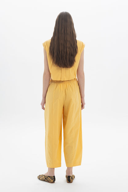 Back view of a woman wearing a yellow cropped sleeveless shirt and matching trousers, showcasing a modern outfit.