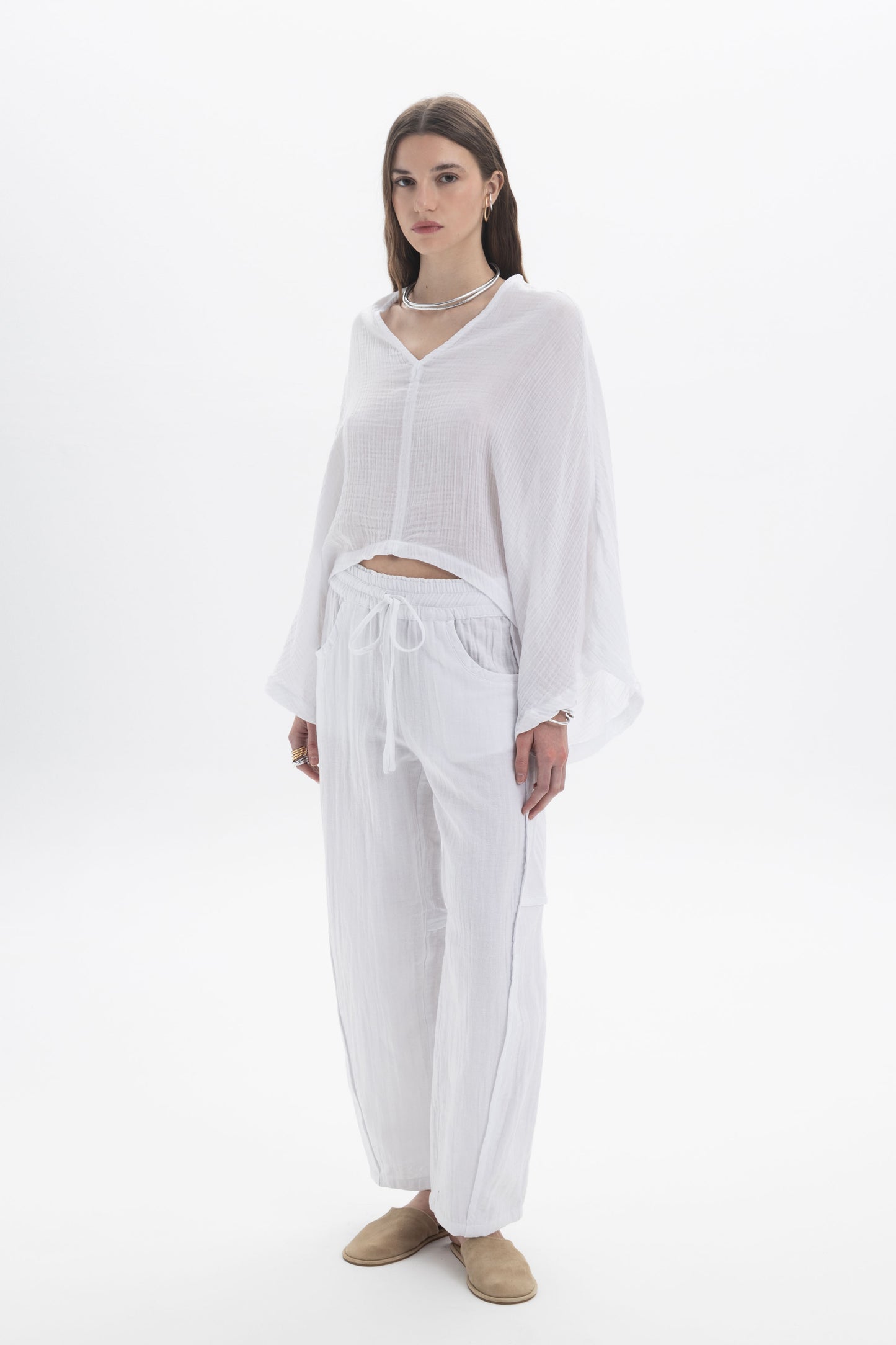 Model wearing a Sheer V-Neck Blouse with wide flowing sleeves and relaxed fit, paired with matching white pants.