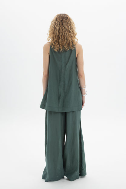 Back view of a woman wearing a green sleeveless bib shirt with a relaxed silhouette and pleat detailing.