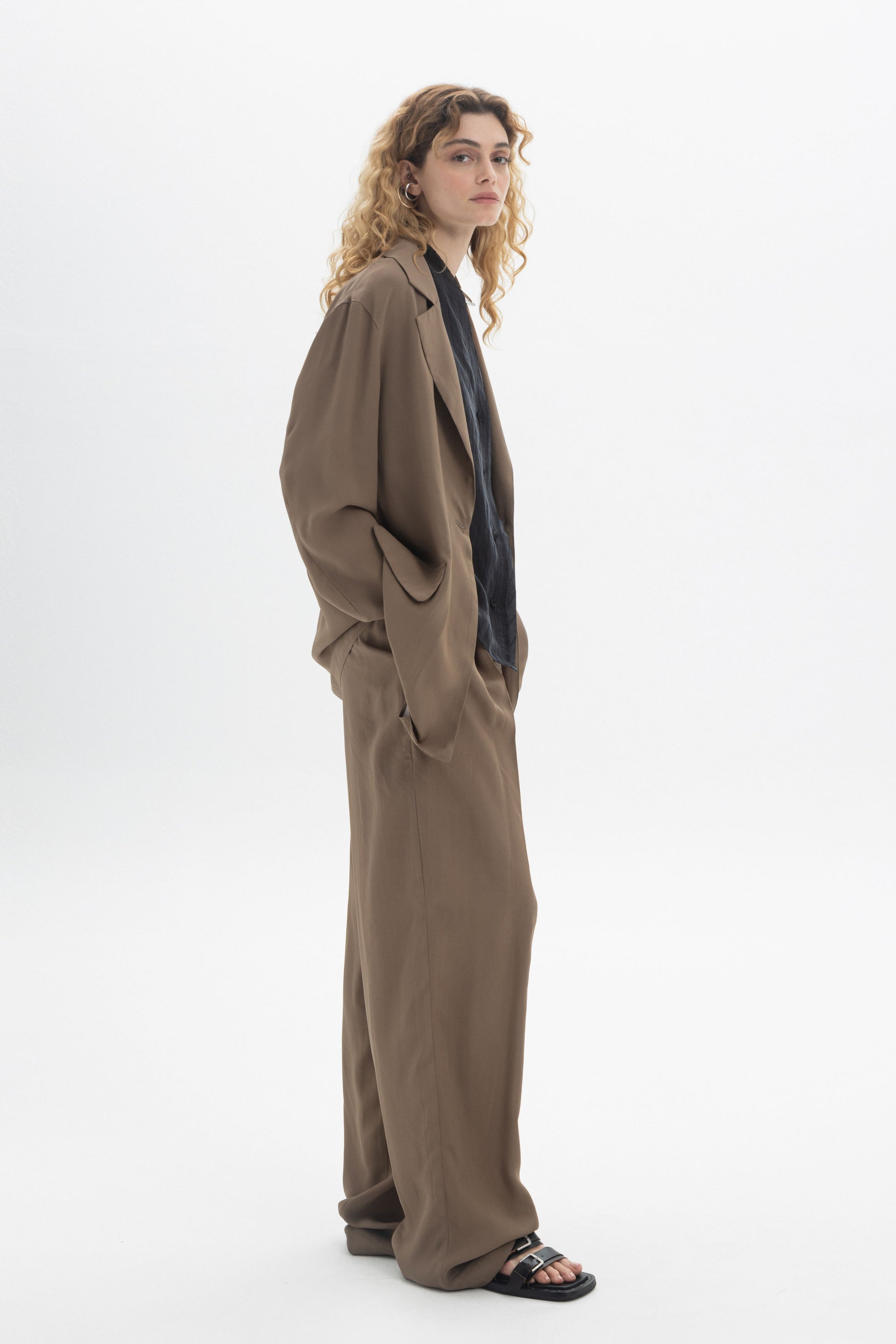 Model wearing Fluid Tailored Trousers with a relaxed fit and soft drape, styled with a dark shirt.