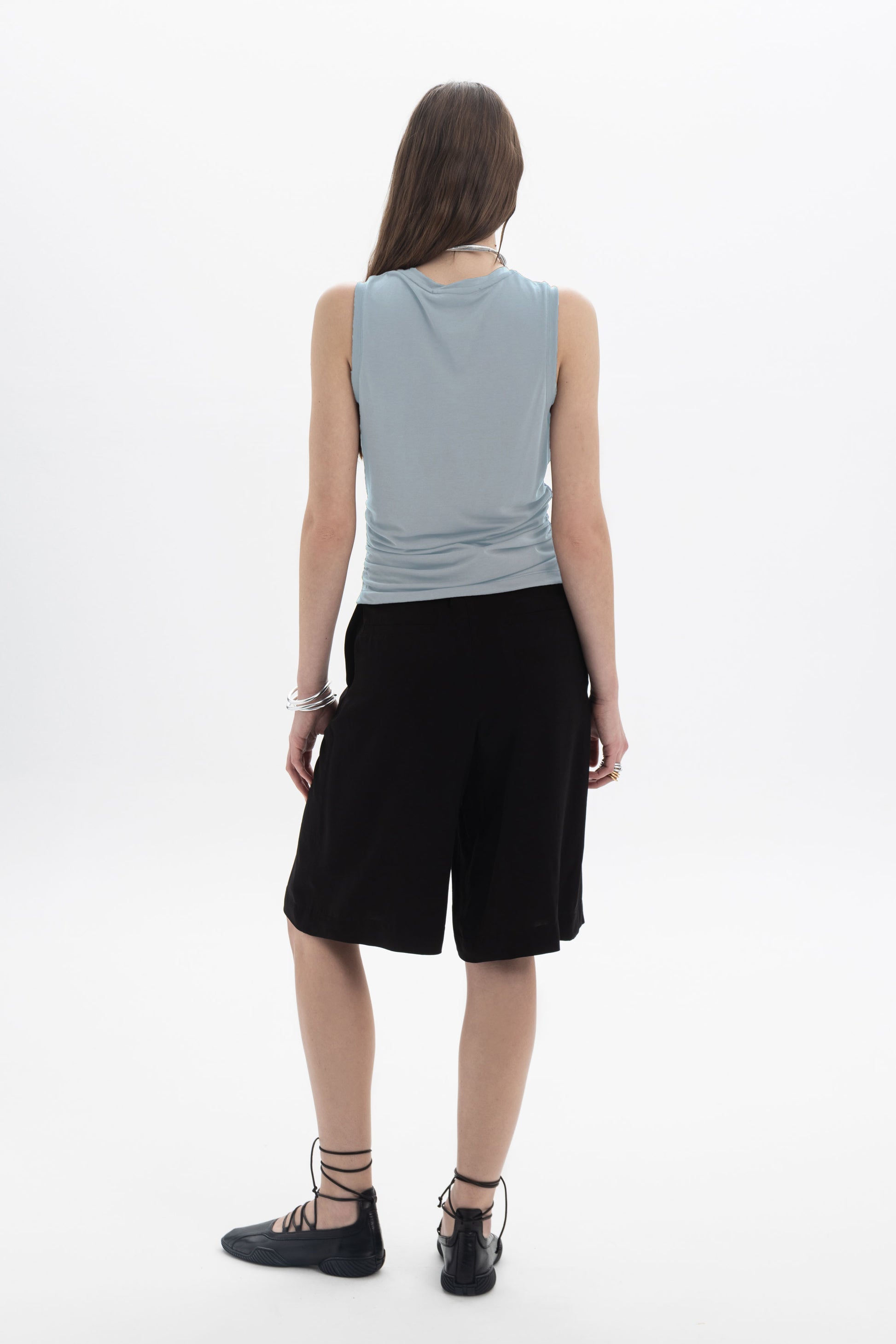 Back view of a model wearing a Ruched Sleeveless Top paired with black shorts.