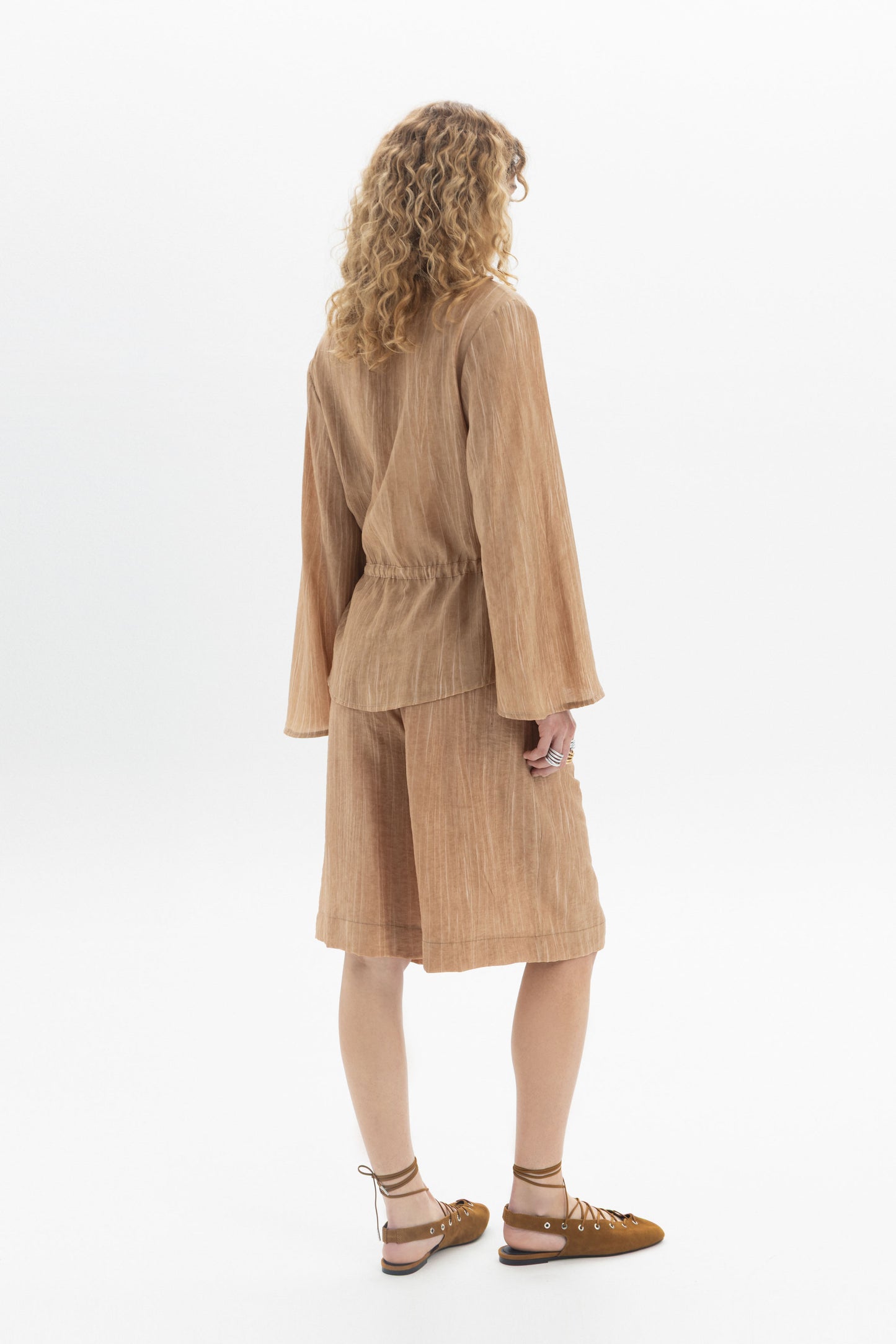 Back view of a woman wearing a Drawstring Waist Blouse with long sleeves and a relaxed fit.