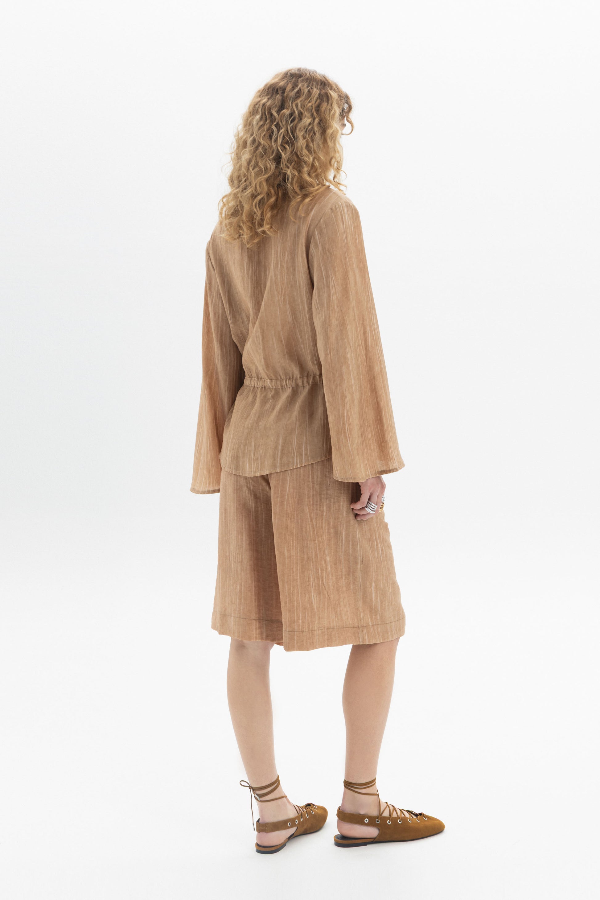 Back view of a woman wearing a Drawstring Waist Blouse with long sleeves and a relaxed fit.