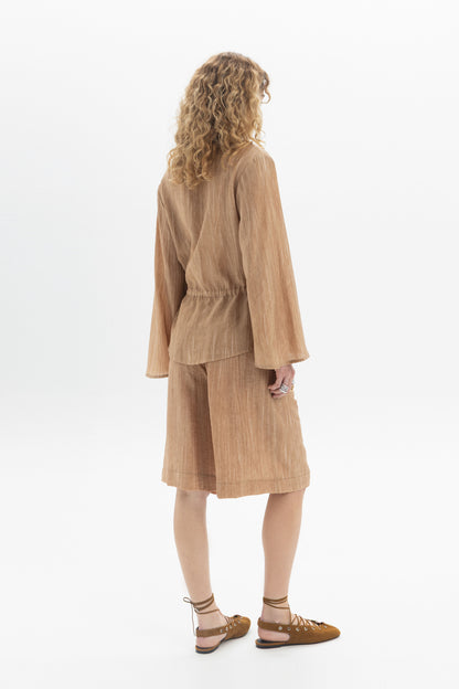 Back view of a woman wearing a Drawstring Waist Blouse with long sleeves and a relaxed fit.