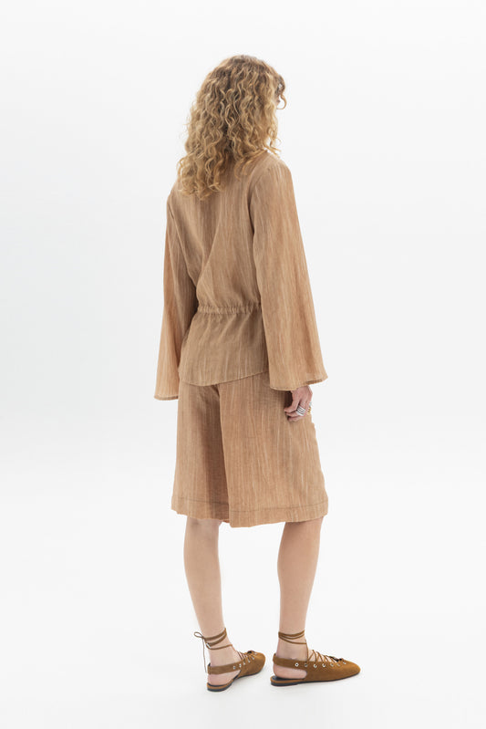 Back view of a woman wearing a Drawstring Waist Blouse with long sleeves and a relaxed fit.