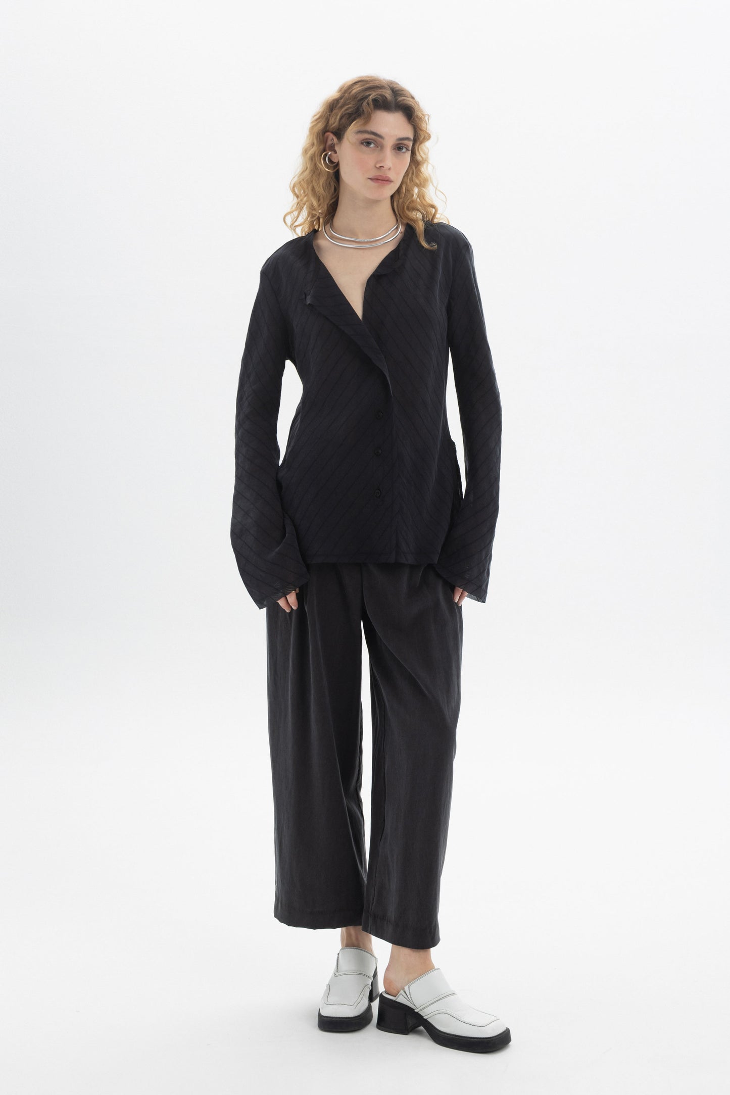 Model wearing a Ruffled V-Neck Blouse with a relaxed fit, styled with wide-leg pants and modern footwear.