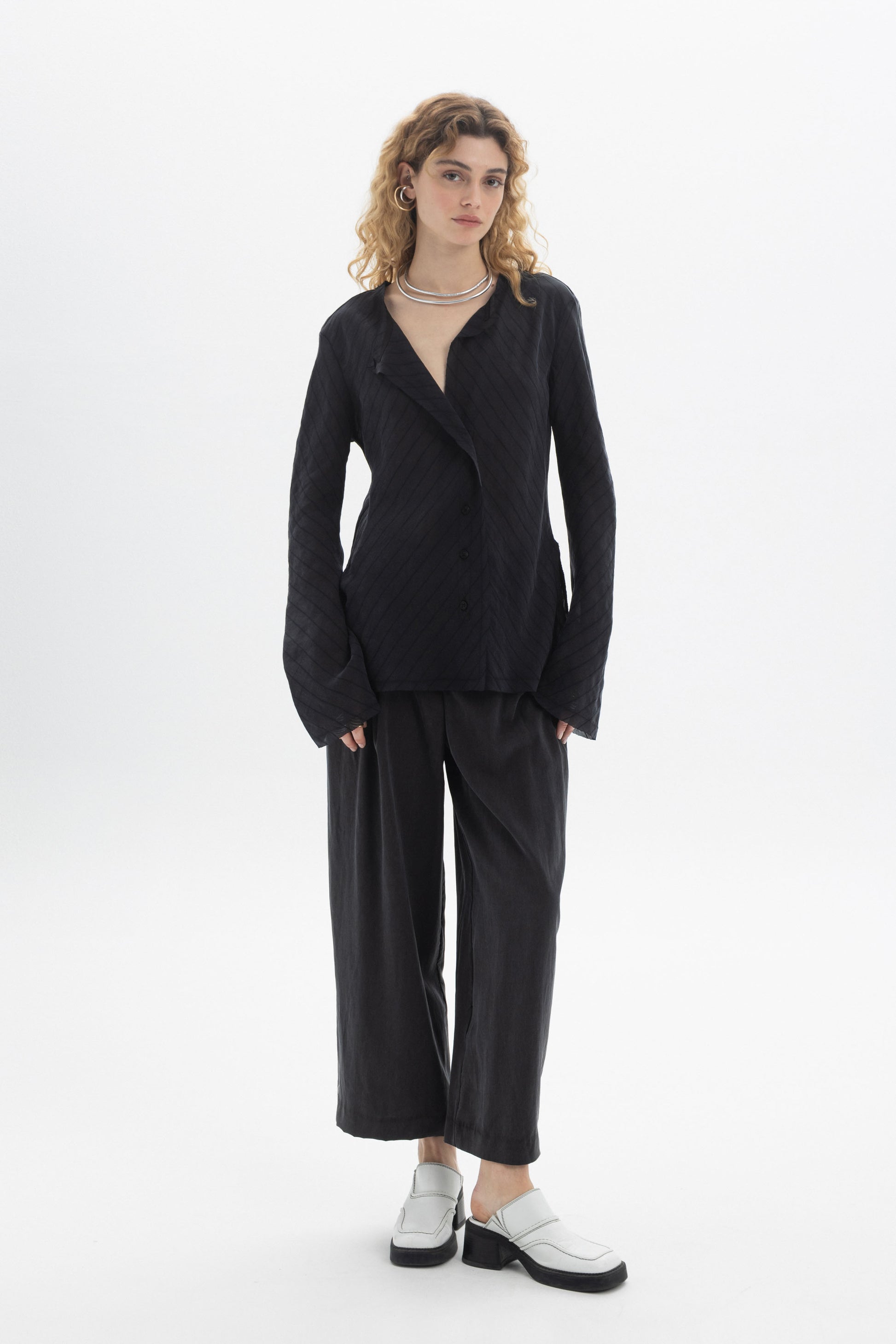 Model wearing a Ruffled V-Neck Blouse with a relaxed fit, styled with wide-leg pants and modern footwear.