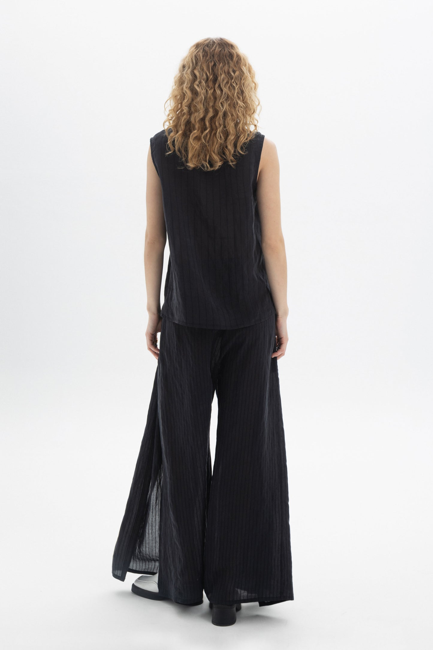 Back view of a model wearing a sleeveless V-Neck Blouse with wide-leg pants in vertical stripes.
