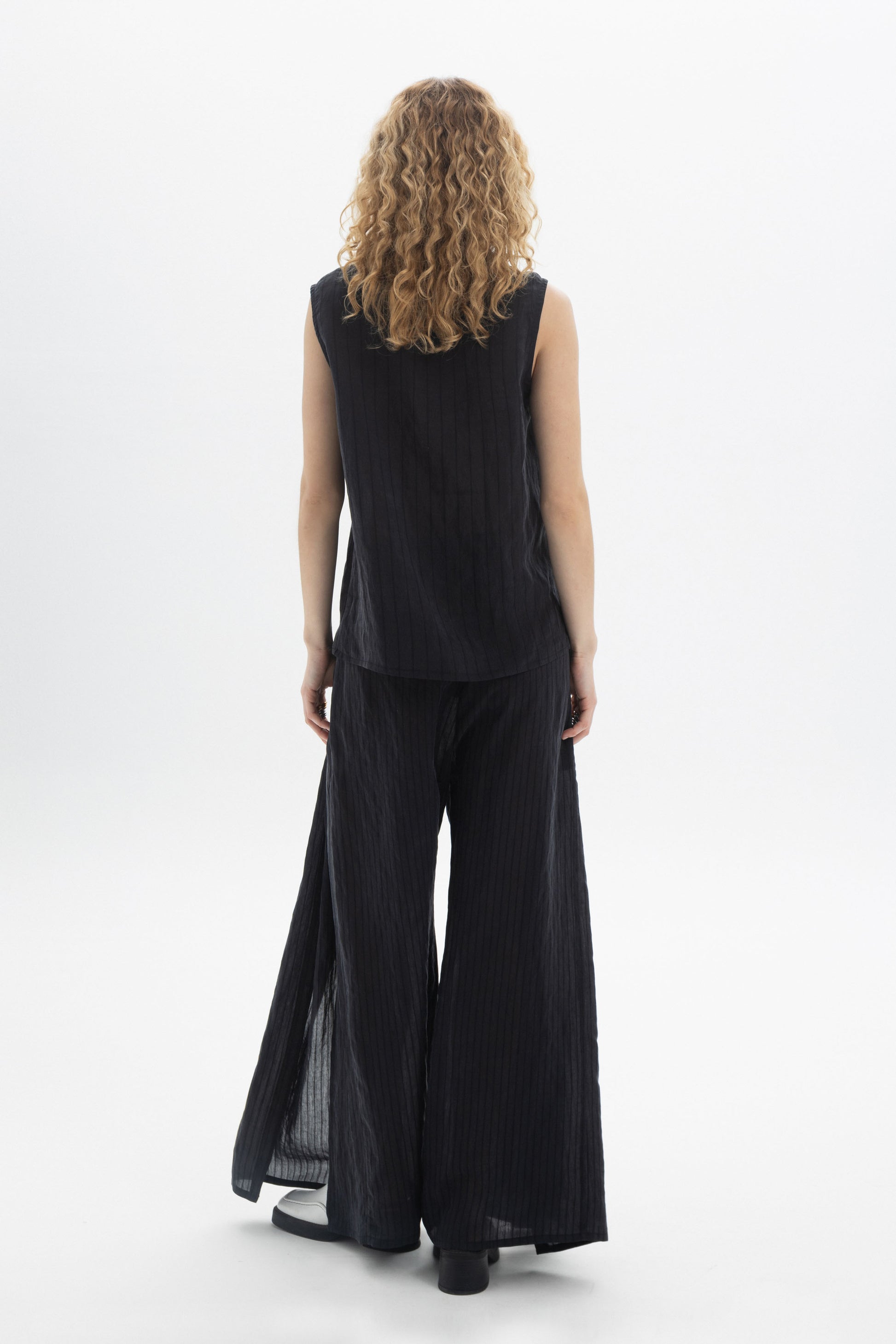 Back view of a model wearing a sleeveless V-Neck Blouse with wide-leg pants in vertical stripes.