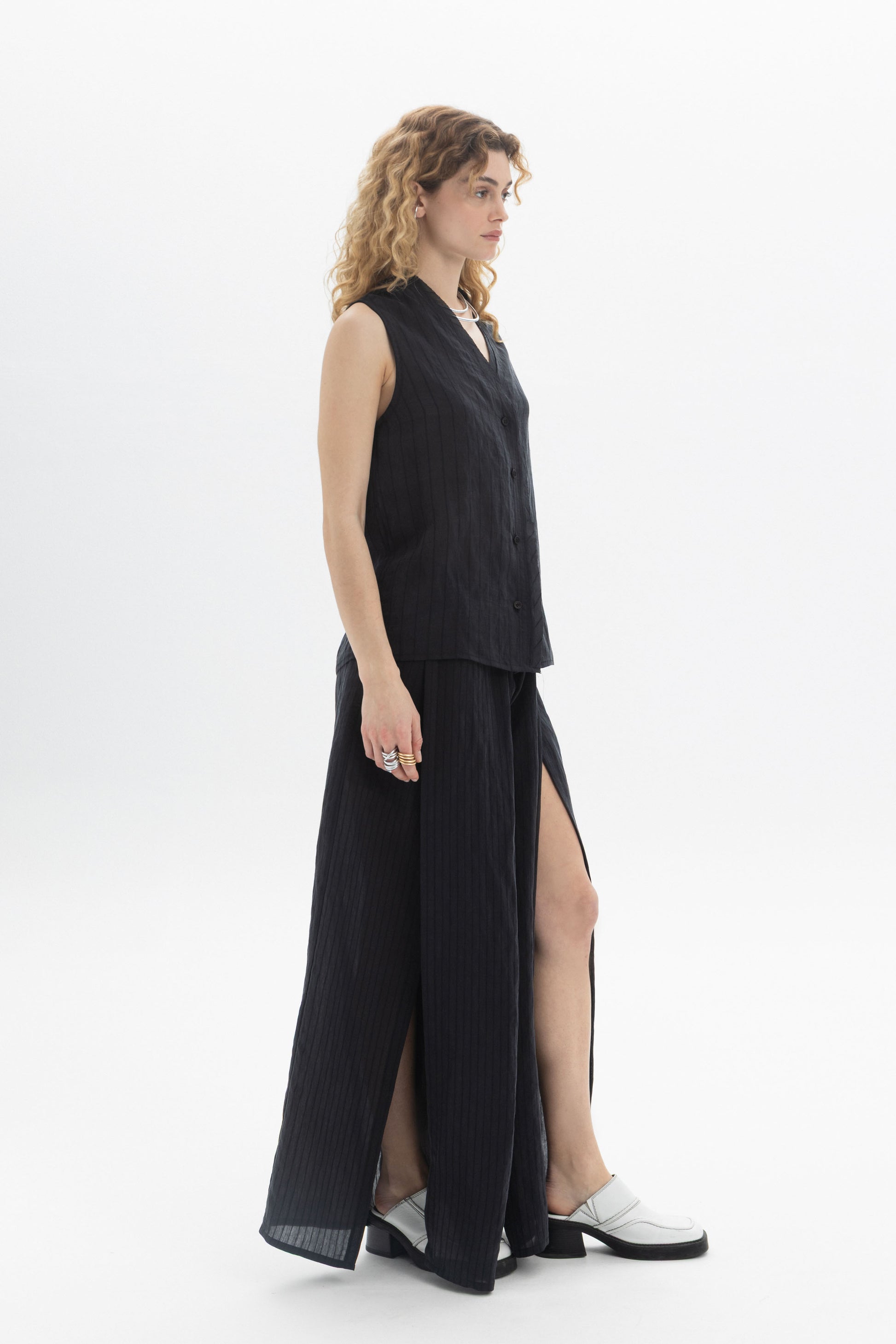 Sleeveless V-Neck Blouse on a model, featuring a button front and fluid structure, styled with a matching skirt.