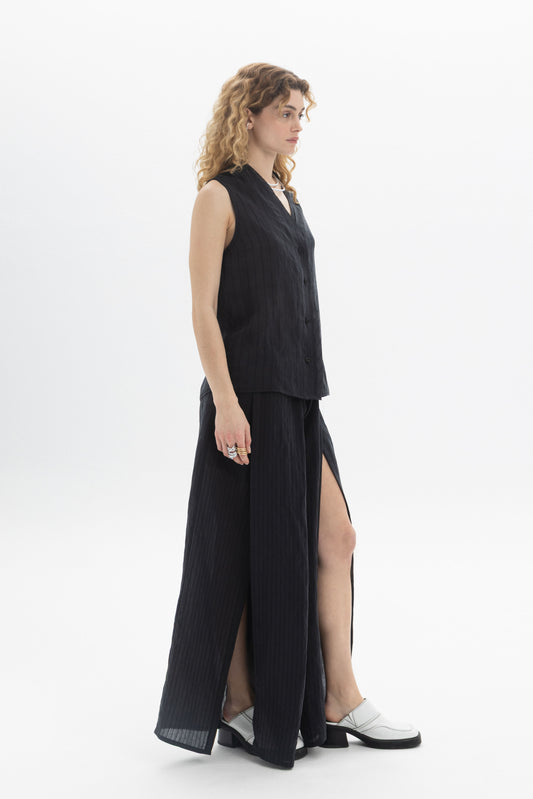 Sleeveless V-Neck Blouse on a model, featuring a button front and fluid structure, styled with a matching skirt.