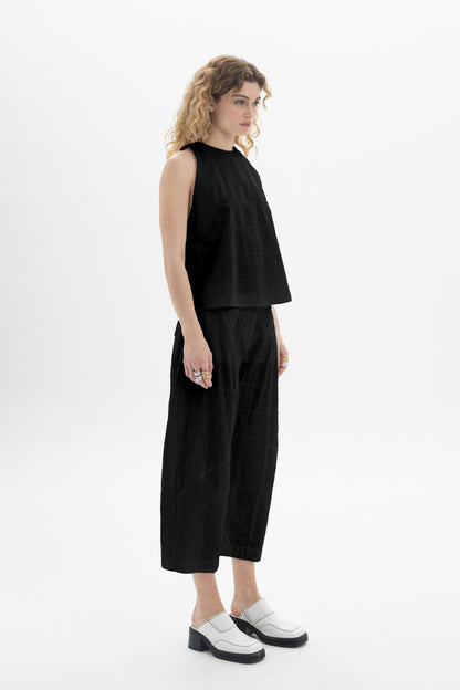 Model wearing a sleeveless high-neck top paired with relaxed-fit black bottoms, showcasing a modern style.