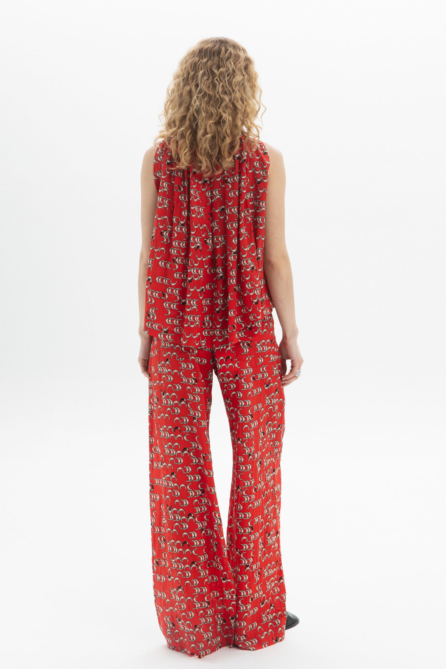 Model wearing a draped high-neck top with fluid drape and pants in a vibrant red pattern.