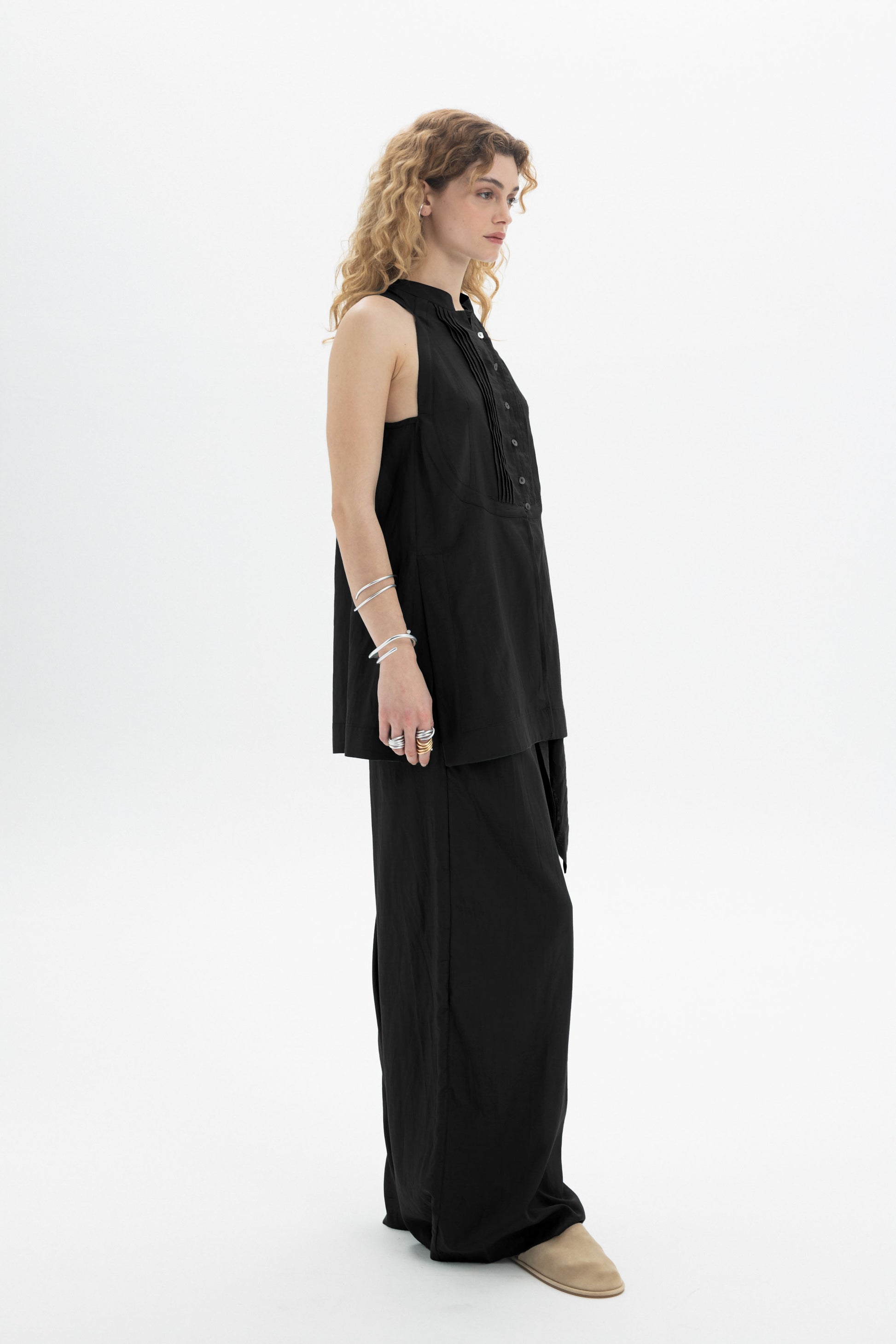 Model wearing a sleeveless bib shirt in black, showcasing button closure and relaxed fit.