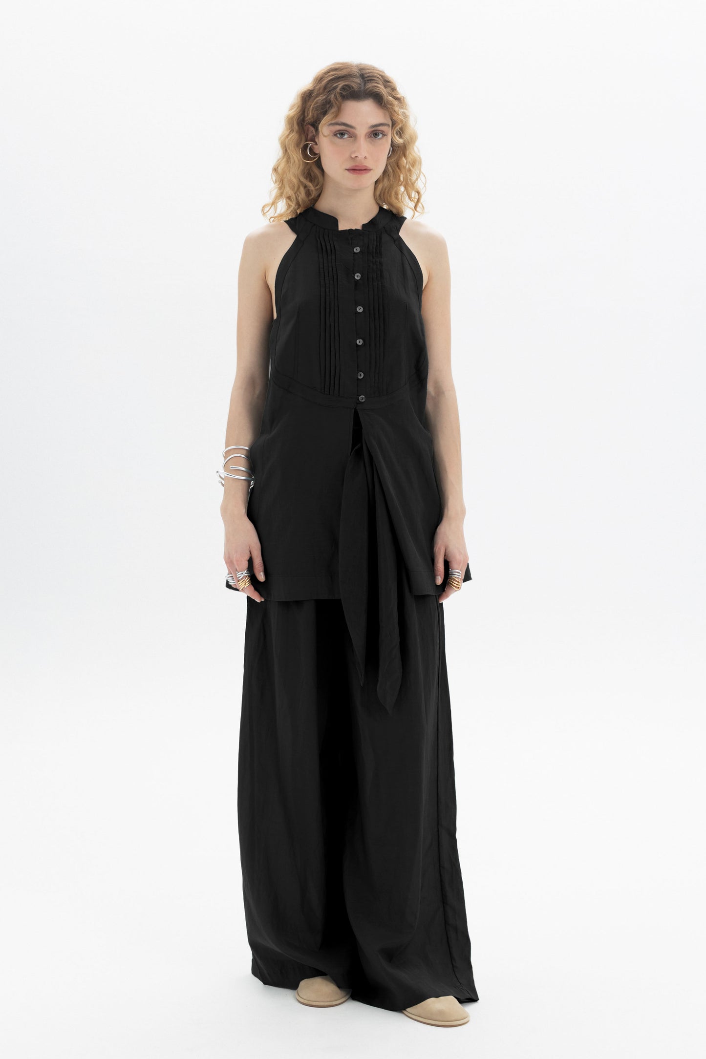 Sleek woman in a black Sleeveless Bib Shirt with pleat detailing and a relaxed silhouette.