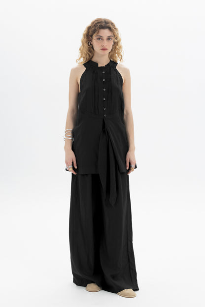 Sleek woman in a black Sleeveless Bib Shirt with pleat detailing and a relaxed silhouette.