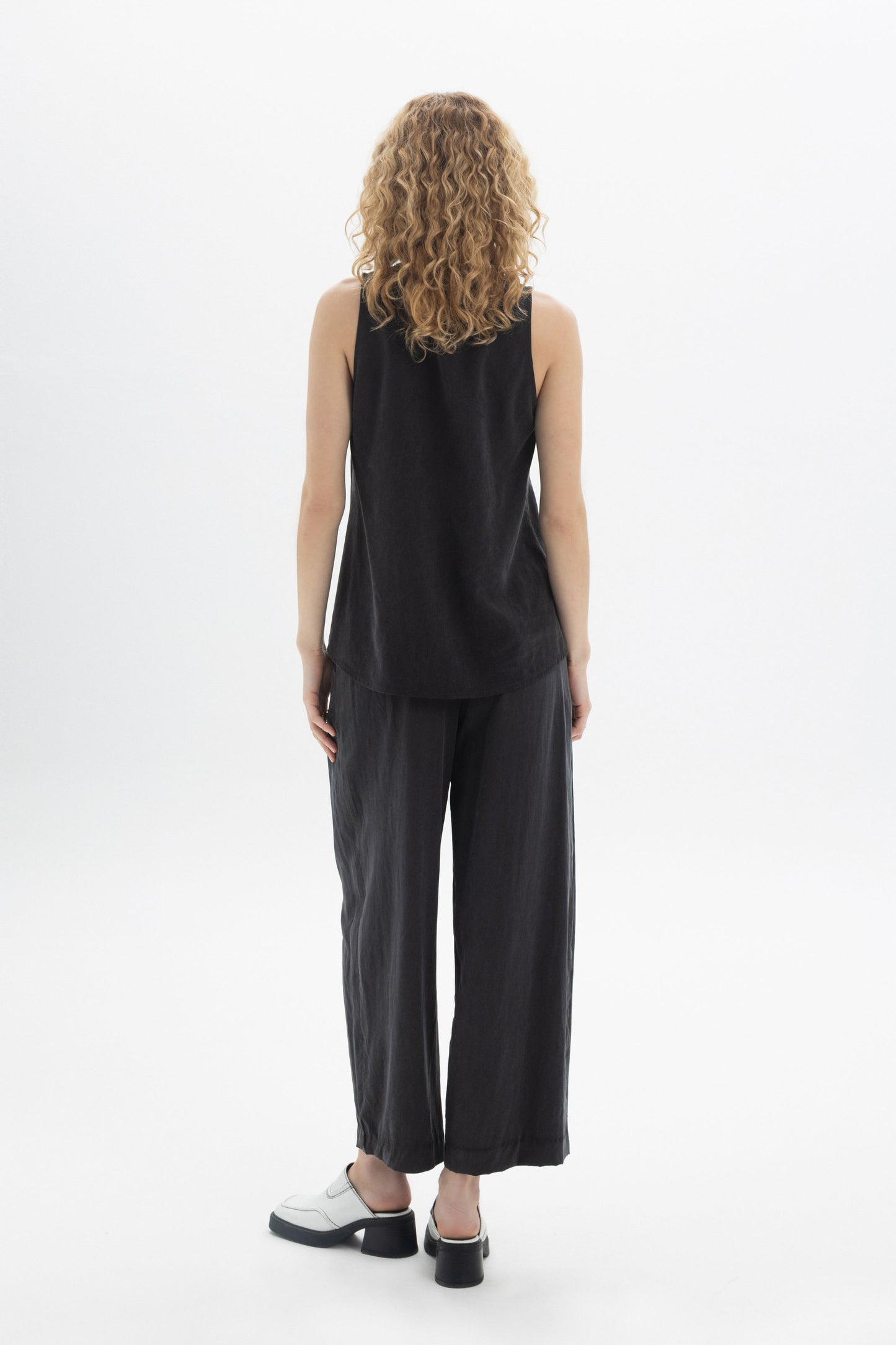 Back view of a model wearing a black Sleeveless Button Top paired with relaxed trousers.